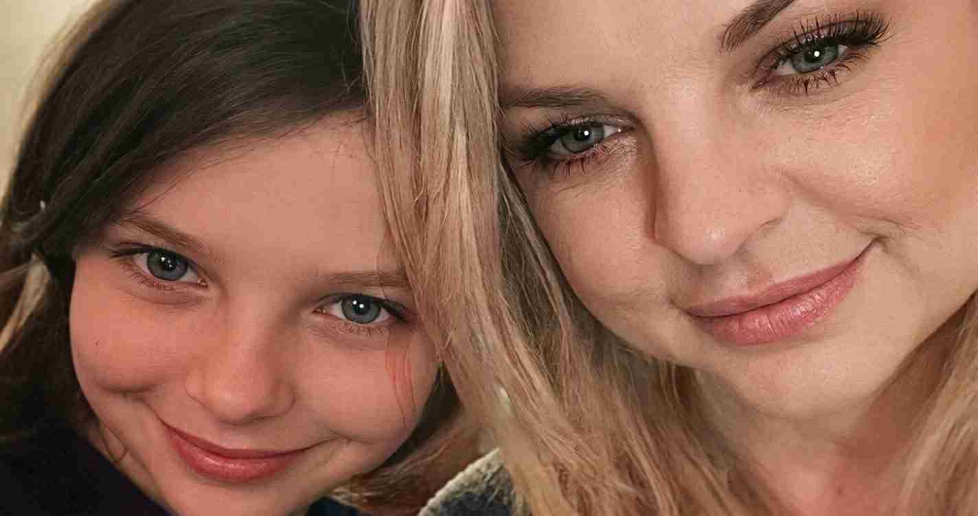 Close-up of two people smiling for a selfie, one with blonde hair and the other with dark hair on the left.