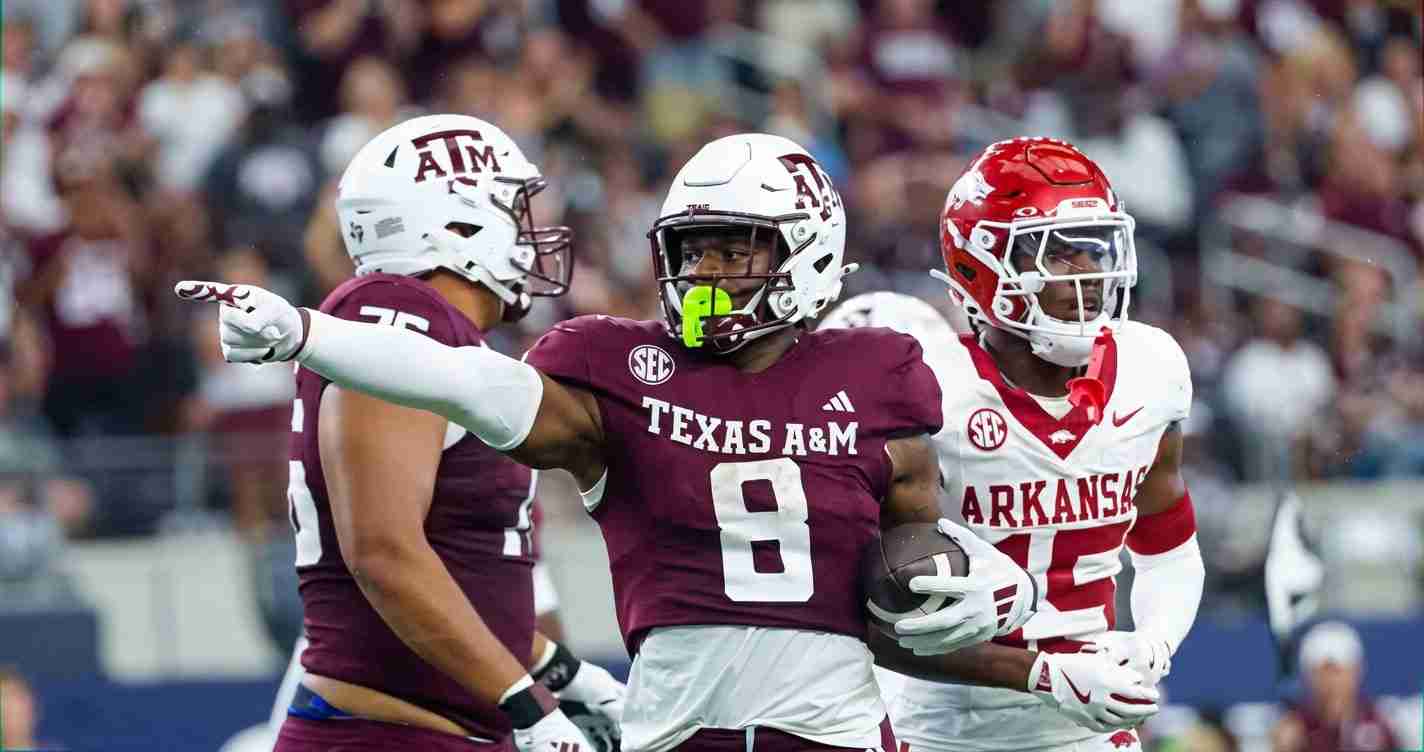 Texas A&M quarterback #8 carrying the ball, pointing as Arkansas defenders approach on the field