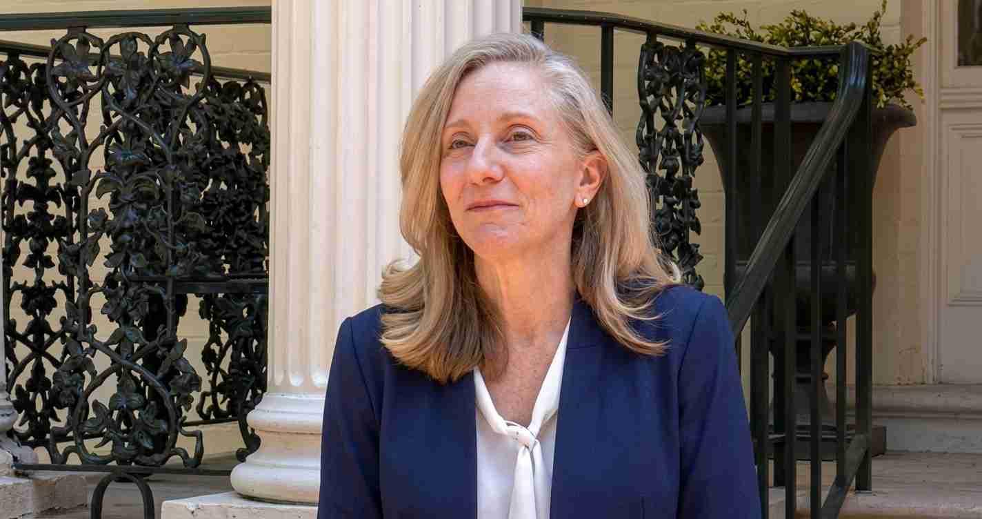 Professional woman in a navy blazer and white blouse stands outside a building with decorative wrought-iron railing.