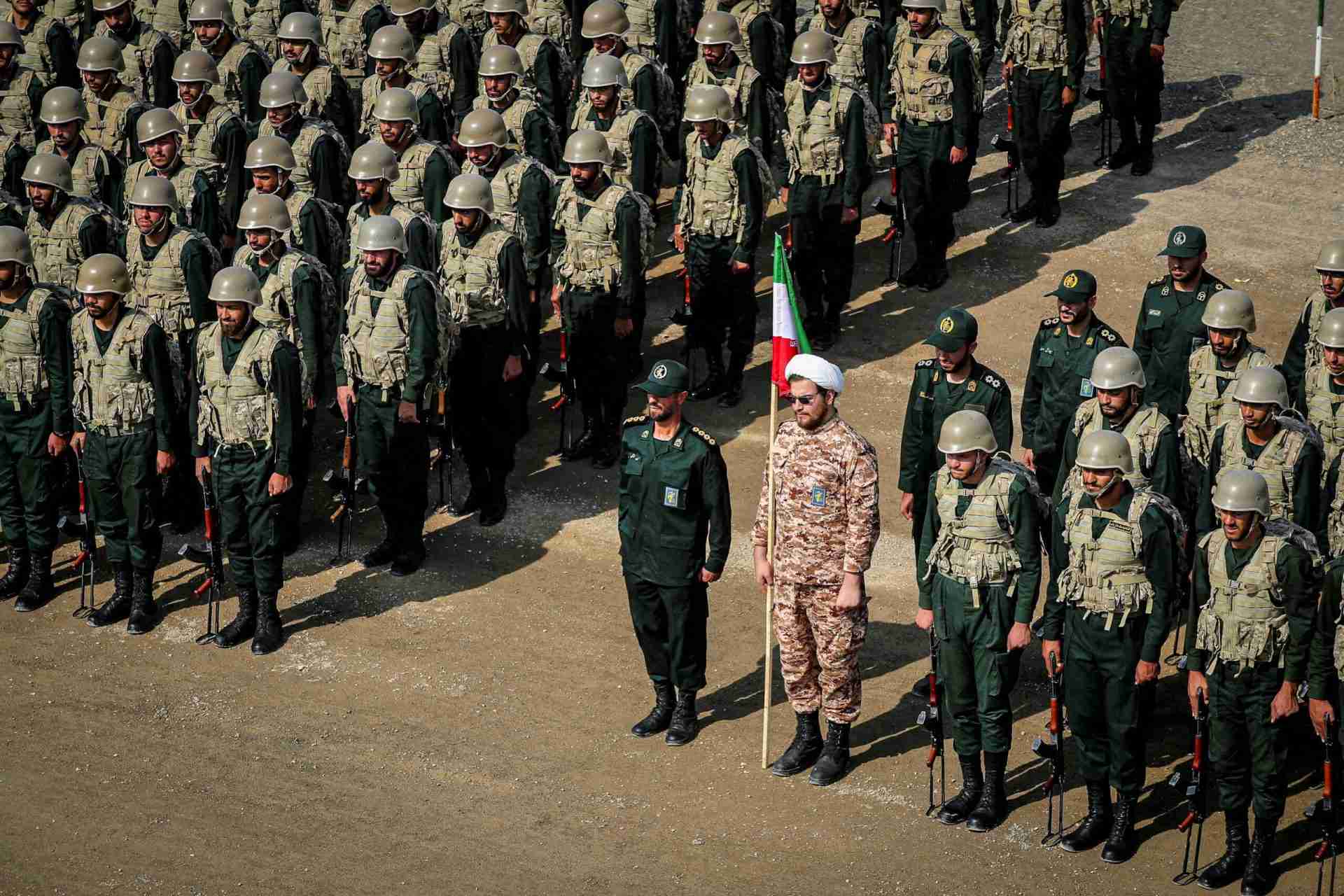 Rows of soldiers in camouflage uniforms and helmets stand at attention in a parade, rifles at their sides.