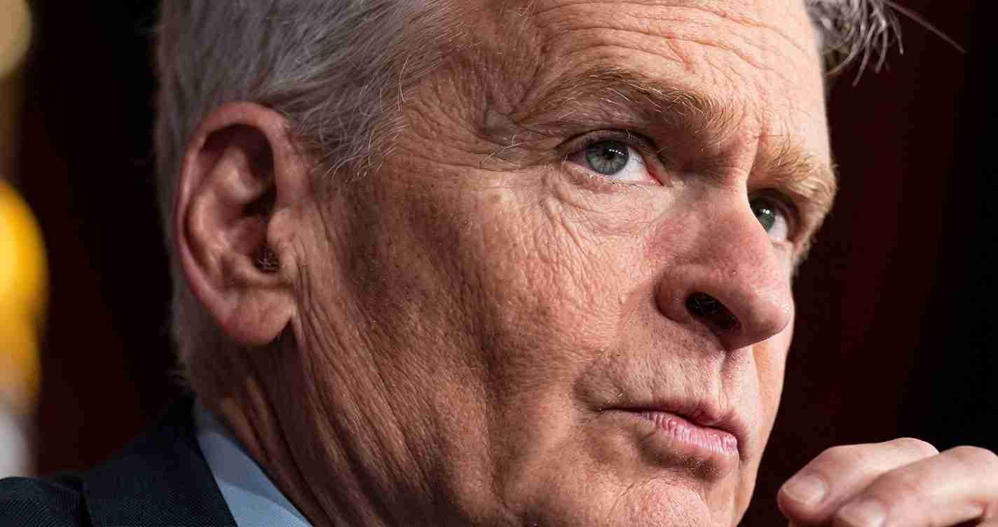 Close-up of a middle-aged man with gray hair and blue eyes, looking to the right with a thoughtful expression.
