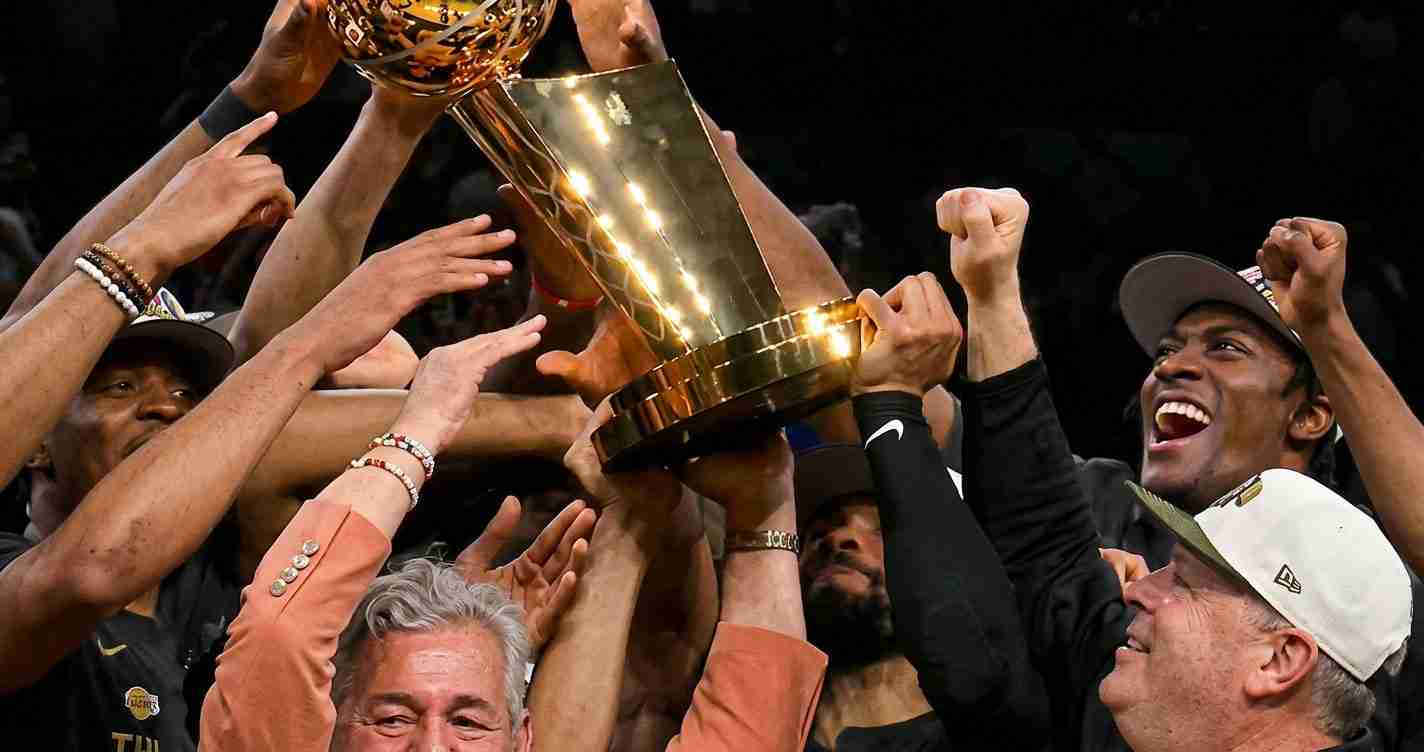 Team of players and staff lift a large gold trophy in celebration above their heads.