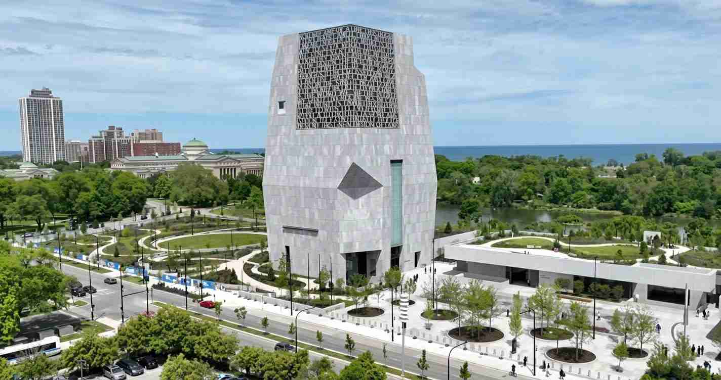 Futuristic grey tower with a lattice grille on top, surrounded by a landscaped plaza and a river in the background.