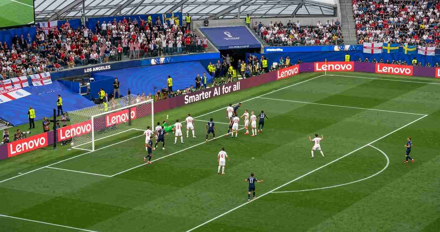 Soccer match near the goal with players contesting the ball as fans watch from the stands and banners around the field.
