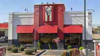 Exterior of a KFC restaurant: red facade, two large red awnings over the windows, and a Colonel Sanders sign above the entrance.