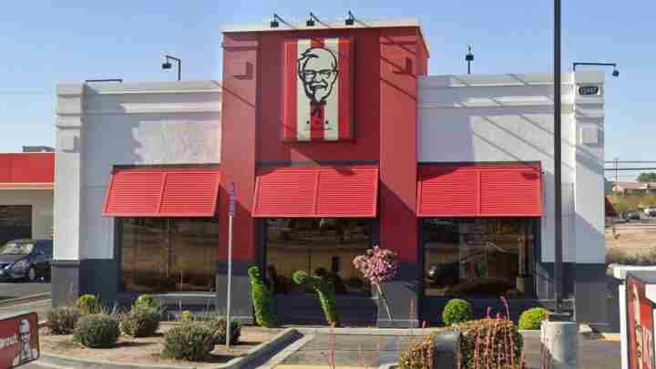 Exterior of a KFC restaurant: red facade, two large red awnings over the windows, and a Colonel Sanders sign above the entrance.