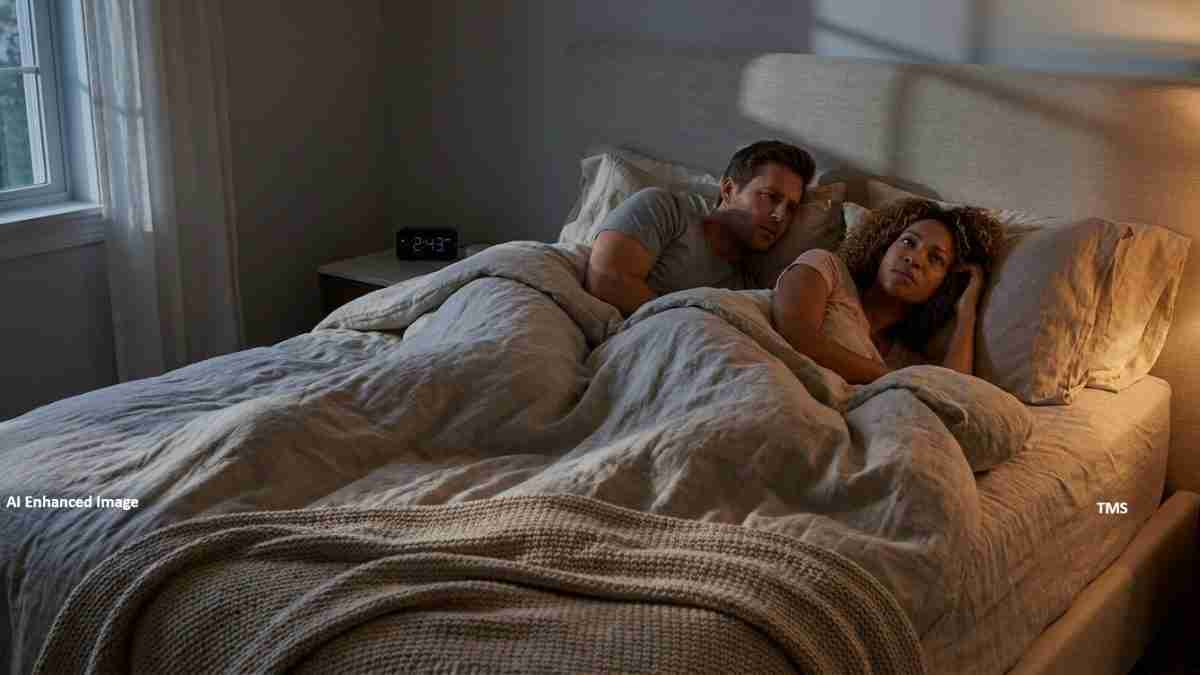 A couple lying in bed together under a gray comforter, facing the camera in a dim morning light by the window, with a clock on the nightstand reading 2:43.