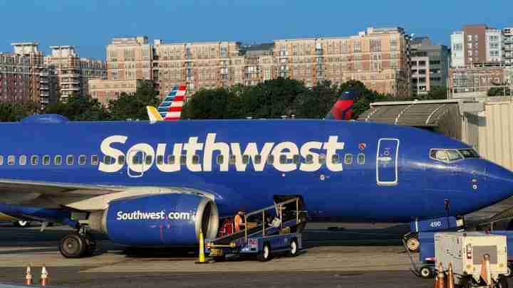 Blue Southwest Airlines jet at the gate with ground crew and boarding stairs nearby.